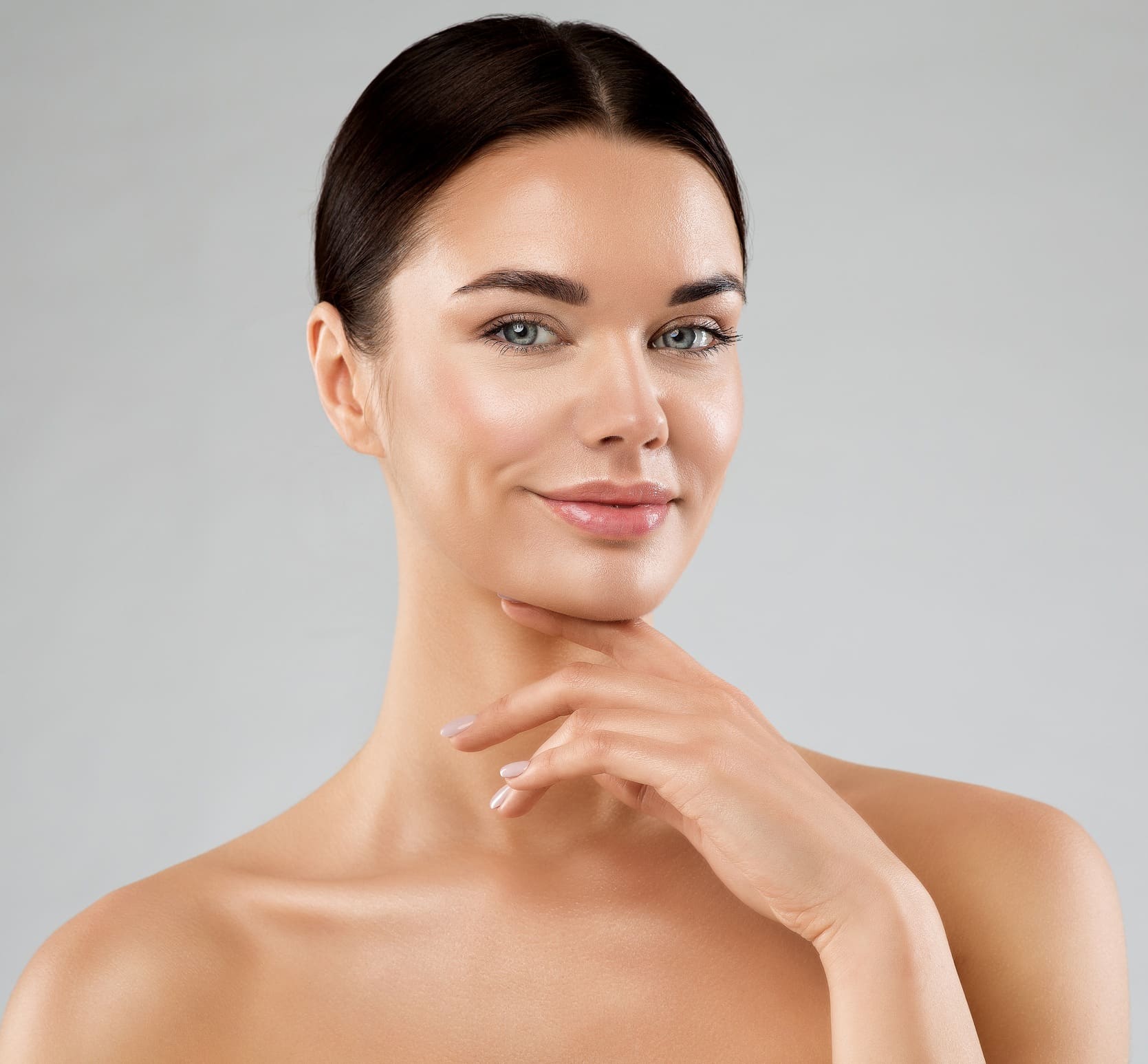 Beauty Model with Smooth Skin touching Chin. Happy Young Woman with Perfect Face Make up over White. Women Facial Spa Cosmetics and Anti Age Cosmetology. Female Plastic Surgery