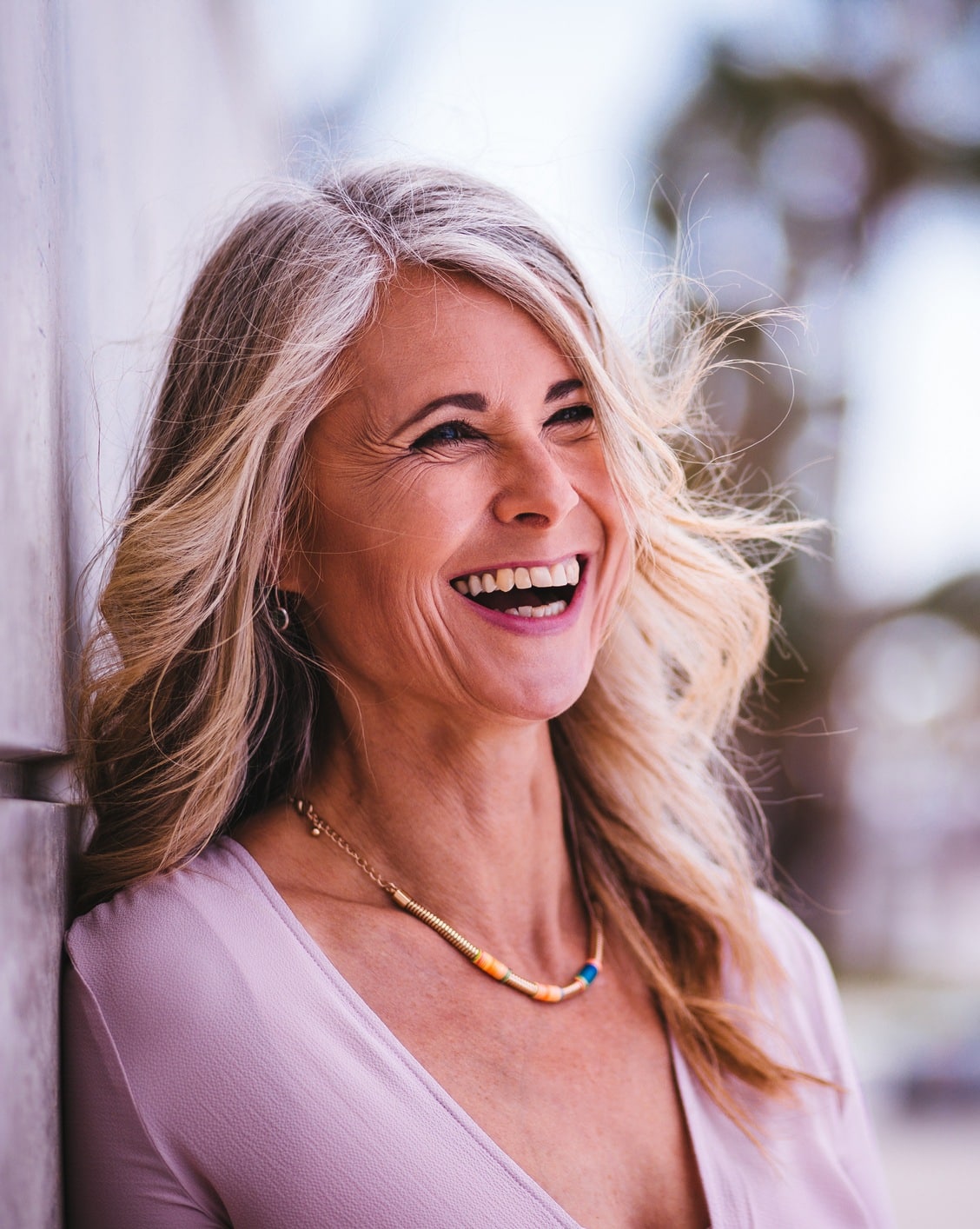Beautiful stylish senior woman laughing leaning against wall outdoors