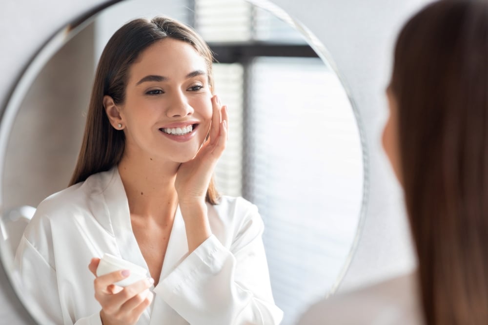Woman looking in the mirror smiling at her clear, flawless skin from Morpheus8 treatments.