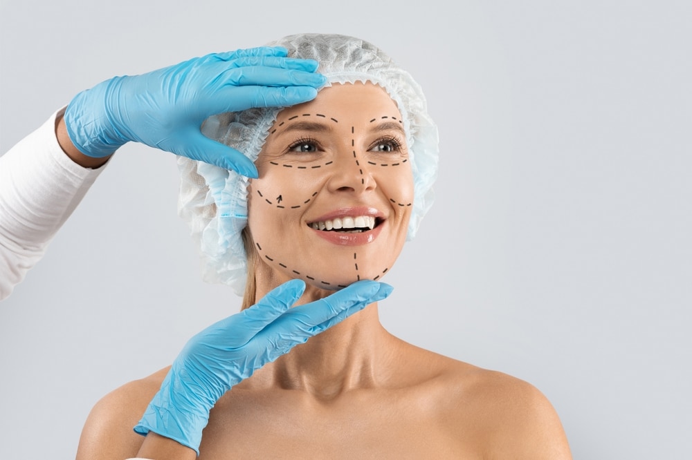 Woman smiling as surgeon's hands examine her face for facial rejuvenation in Salt Lake City