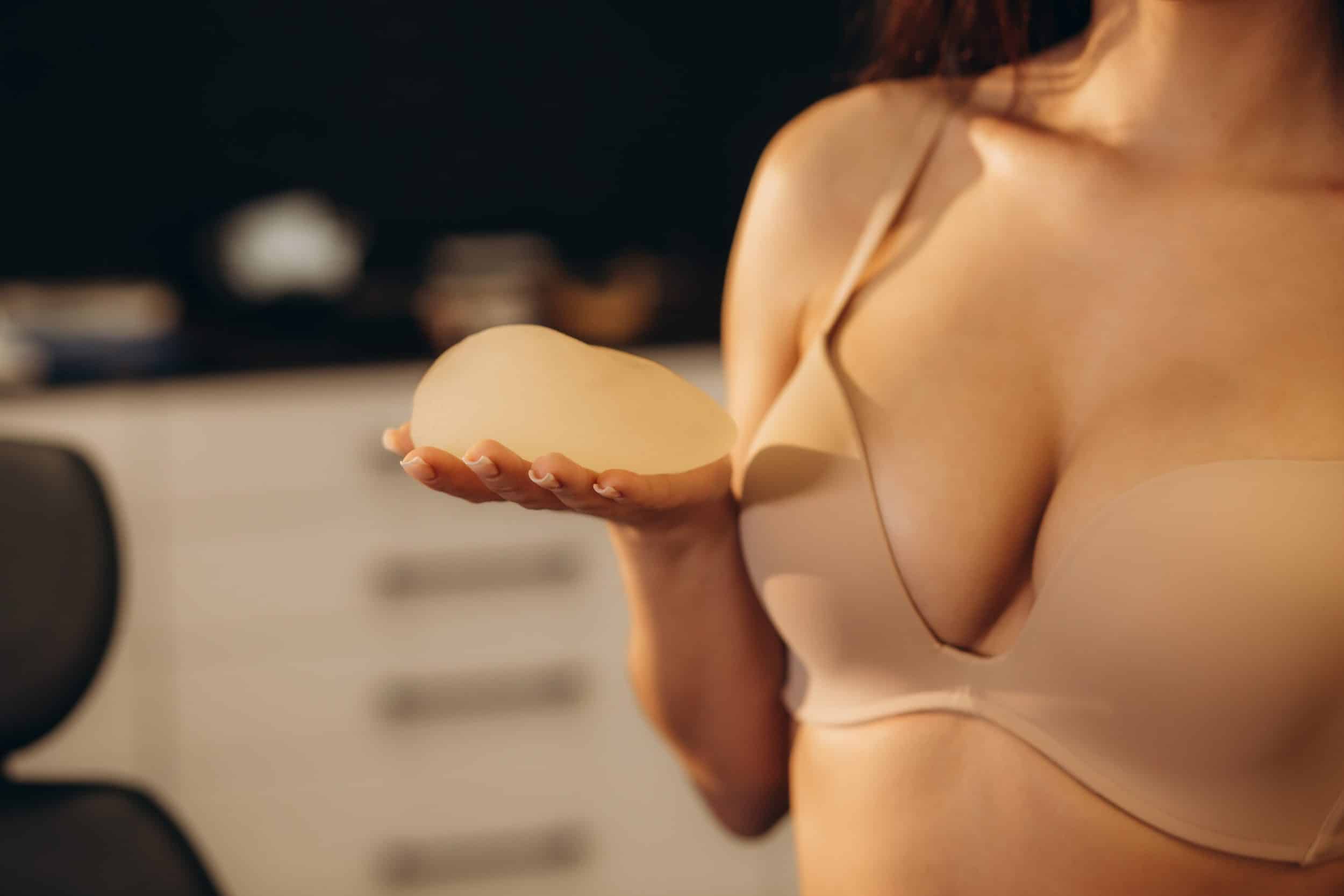 Woman in a bra holding a breast implant considering breast implant revision in Salt Lake City, UT