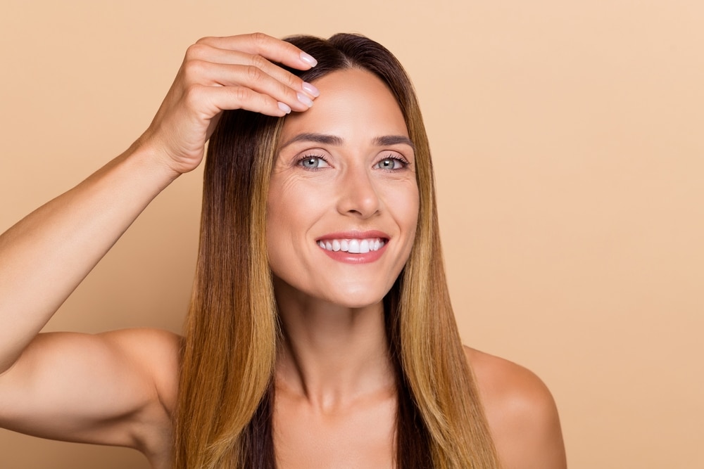 Woman smiling touching her face, needing a facelift in Salt Lake City, UT